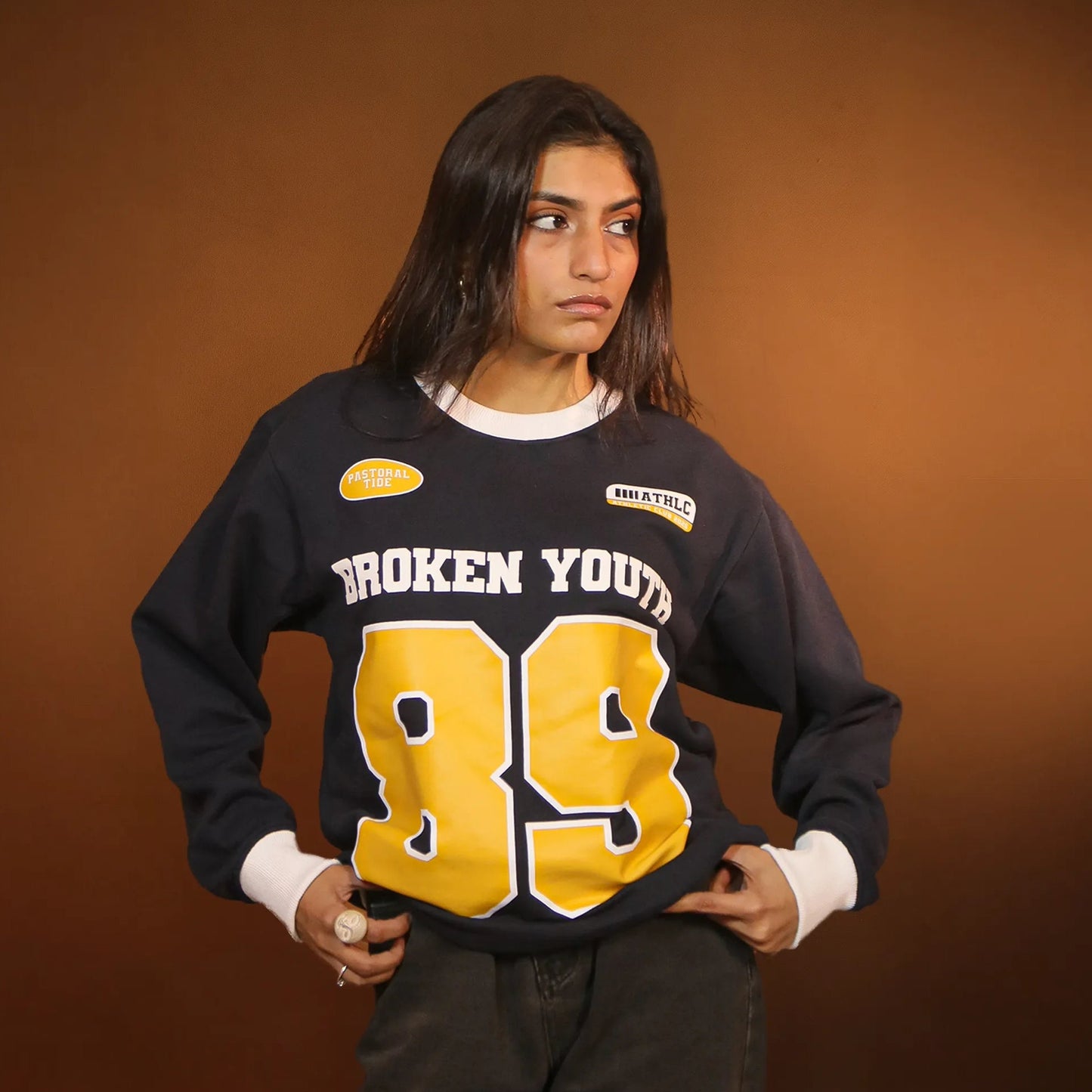 Person wearing a black sweatshirt with 'Broken Youth 89' text and graphics on a brown background