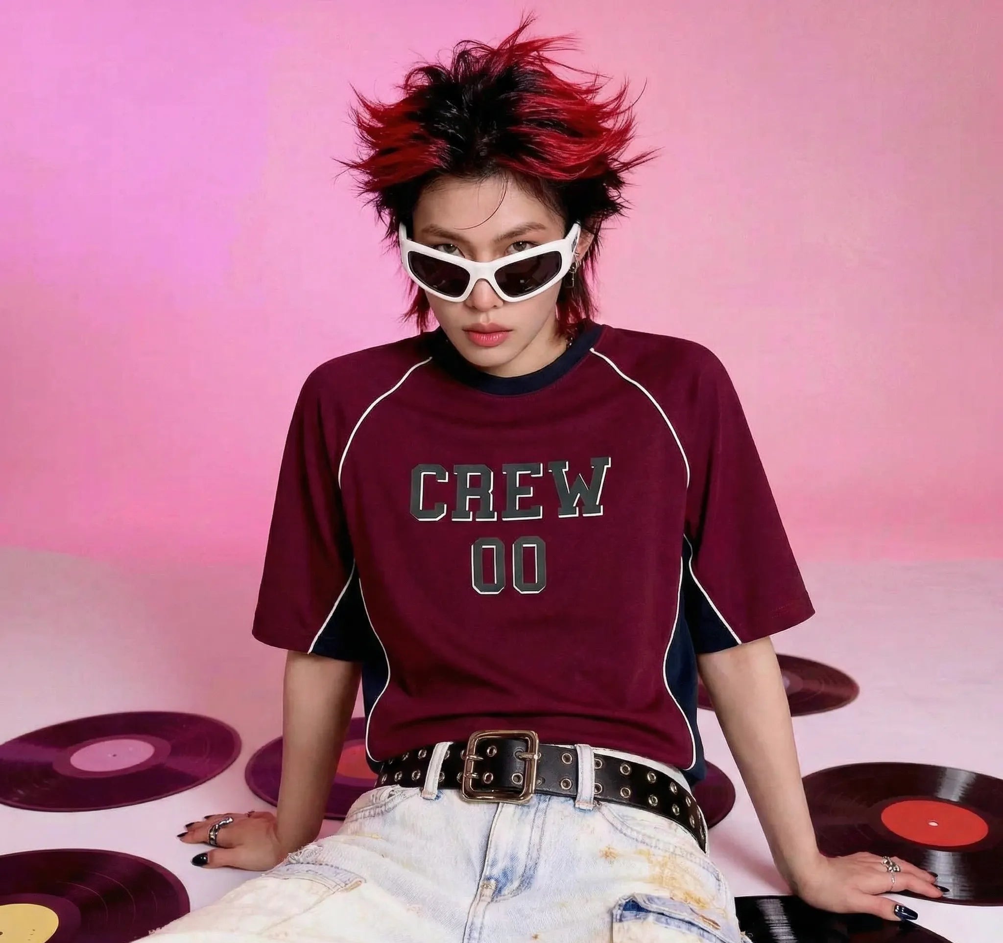 Person wearing a maroon 'CREW 00' t-shirt with vinyl records on a pink background